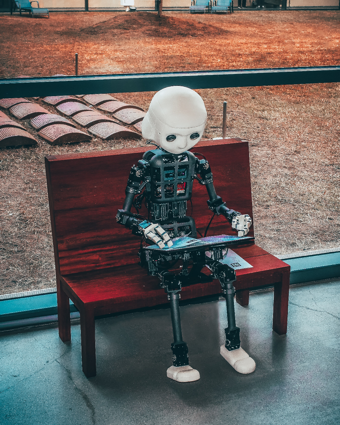 A little boy robot sitting on a bench playing a game