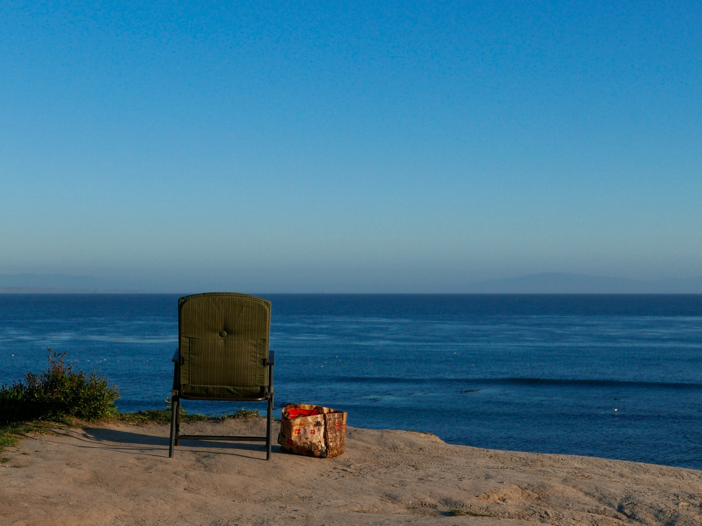 A chair and a bag on a hilll overlooking a blue ocean