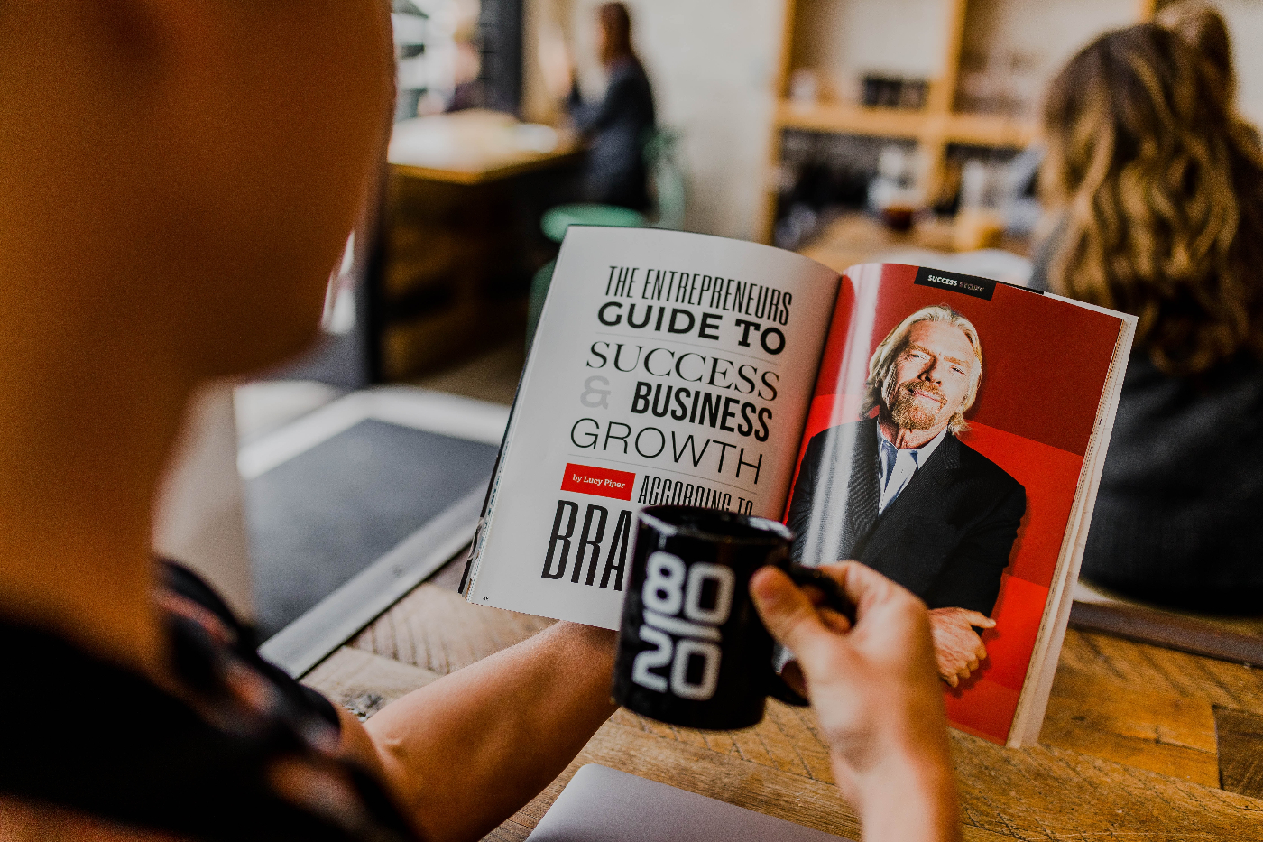 a kid holding a black 8020 mug while looking at an article about Richard Branson