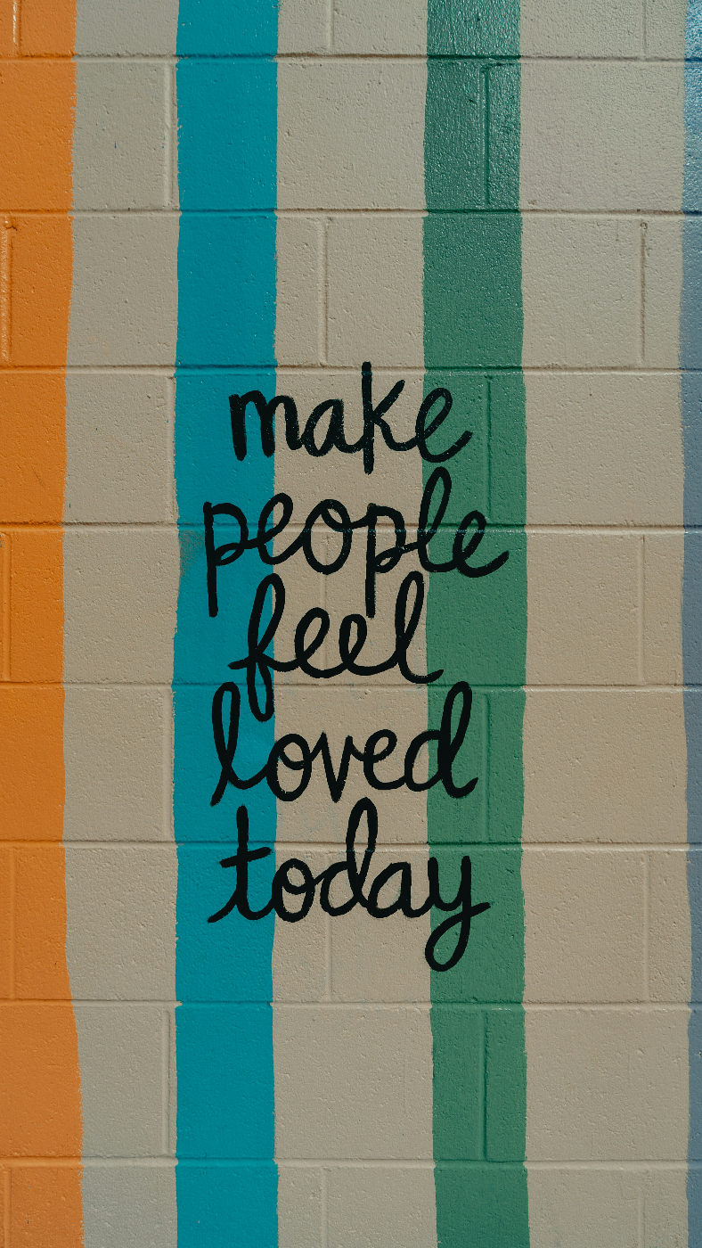 A white wall with one orange, one blue and one green stripe and the words Make people Feel Loved Today