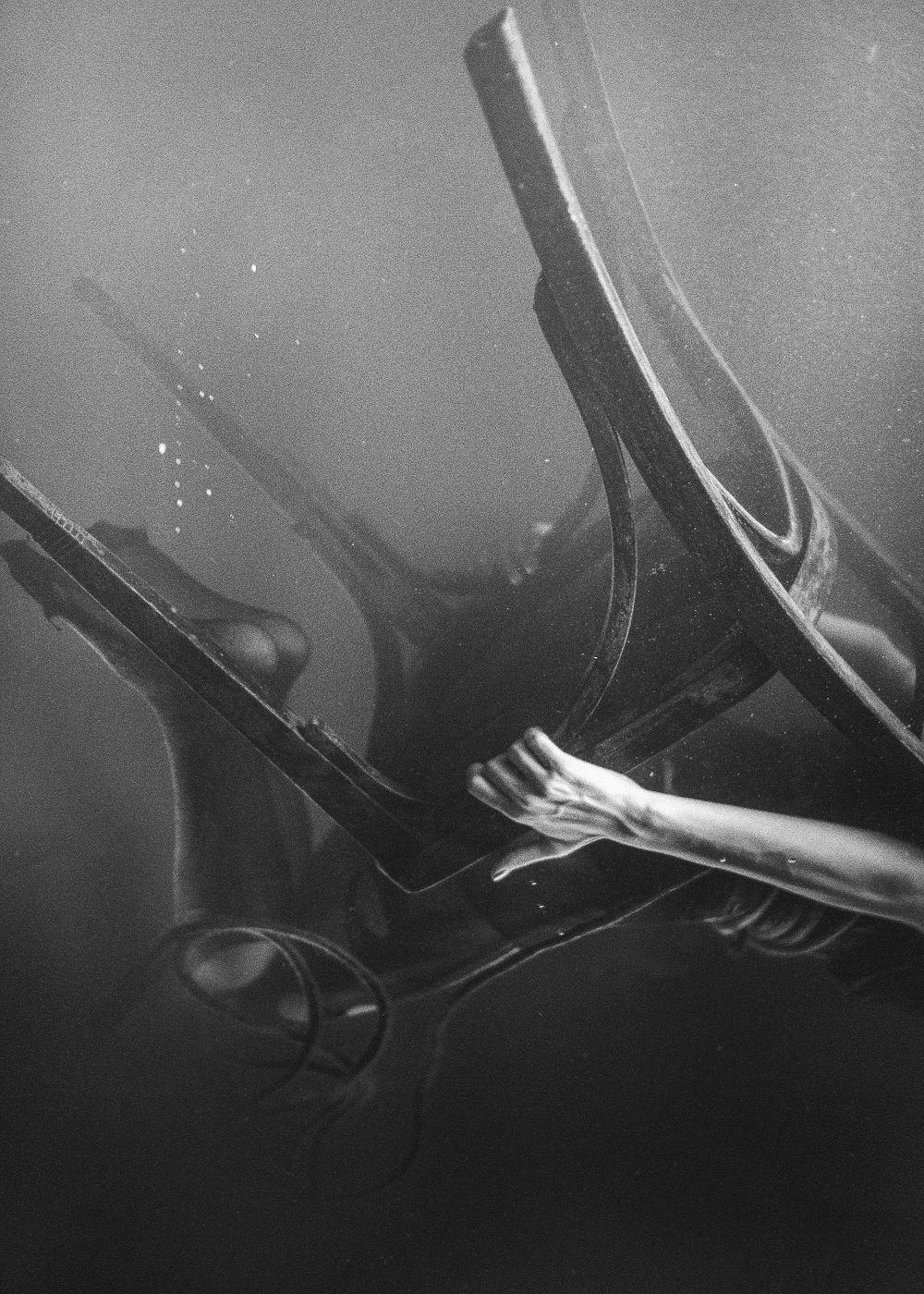 A woman seated and holding on to a cane back chair as it sinks beneath the water