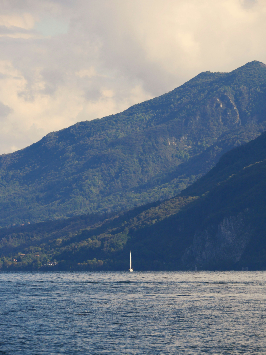 A panoramic view of mountains, the ocean and a tiny sailboat in the midst