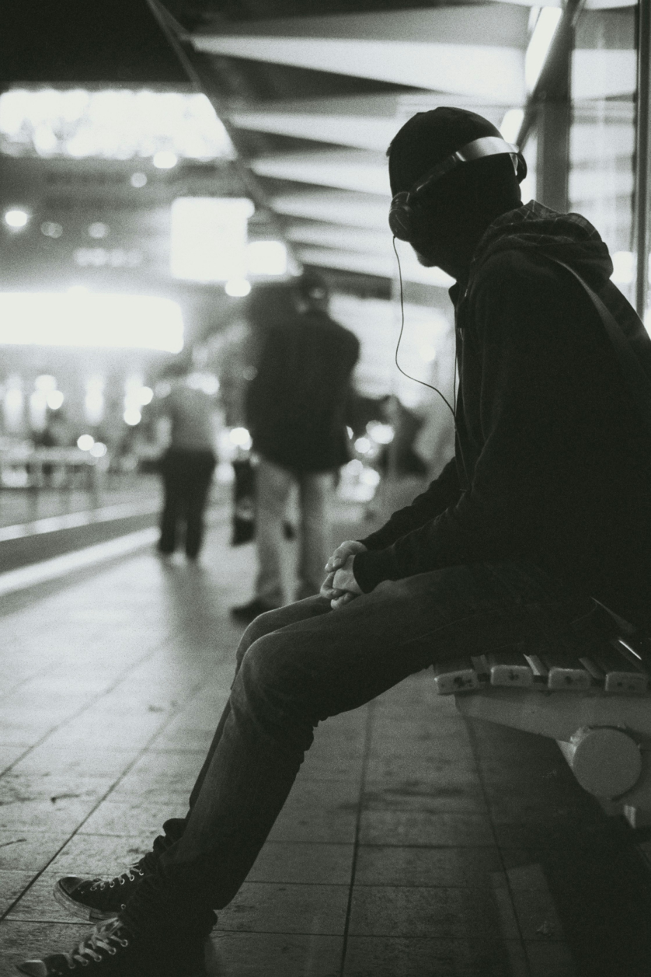 Grey scale, man in a hoodie with headphones waiting in a train station