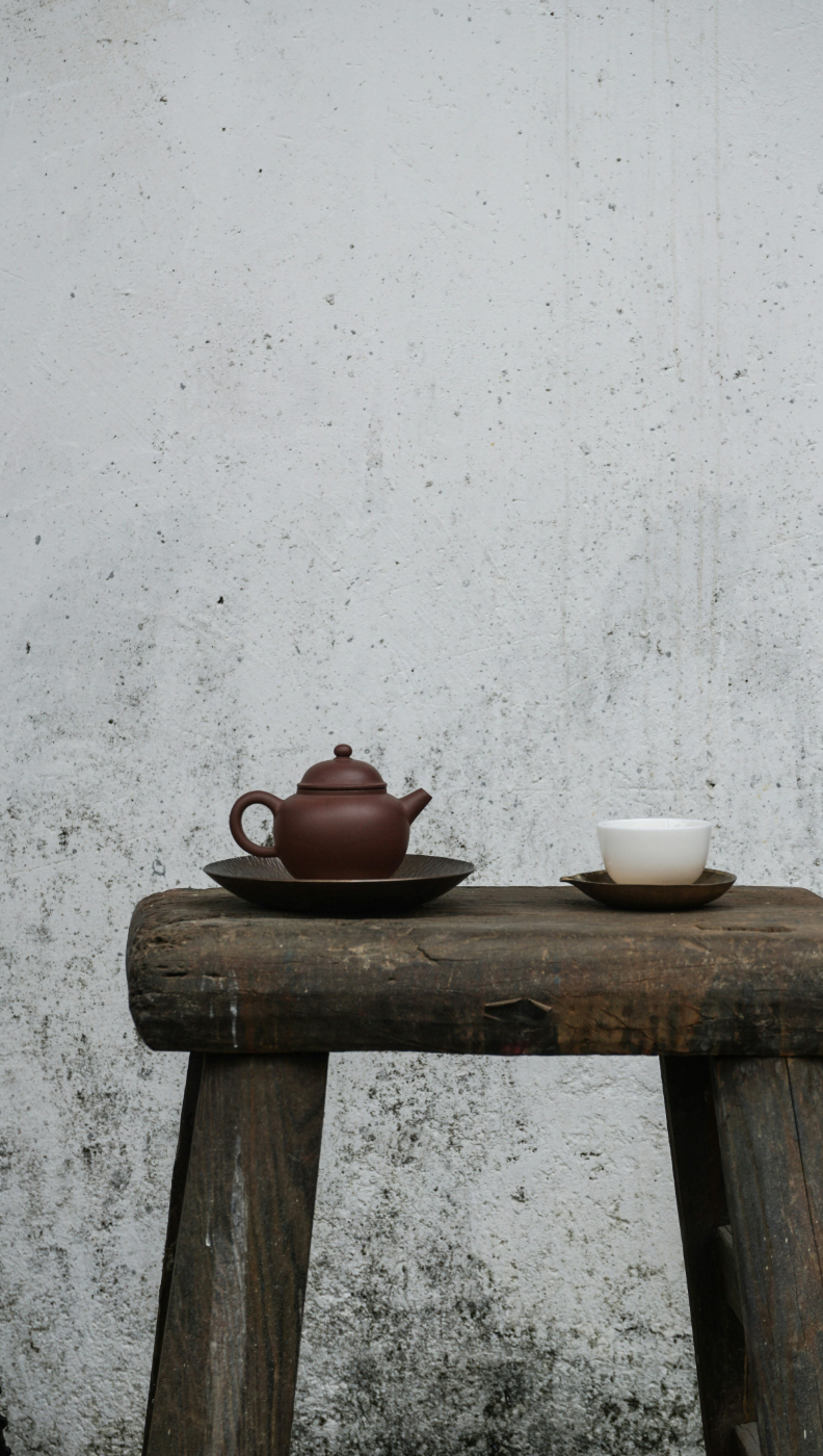 A small table with a brown tea pot and white cup