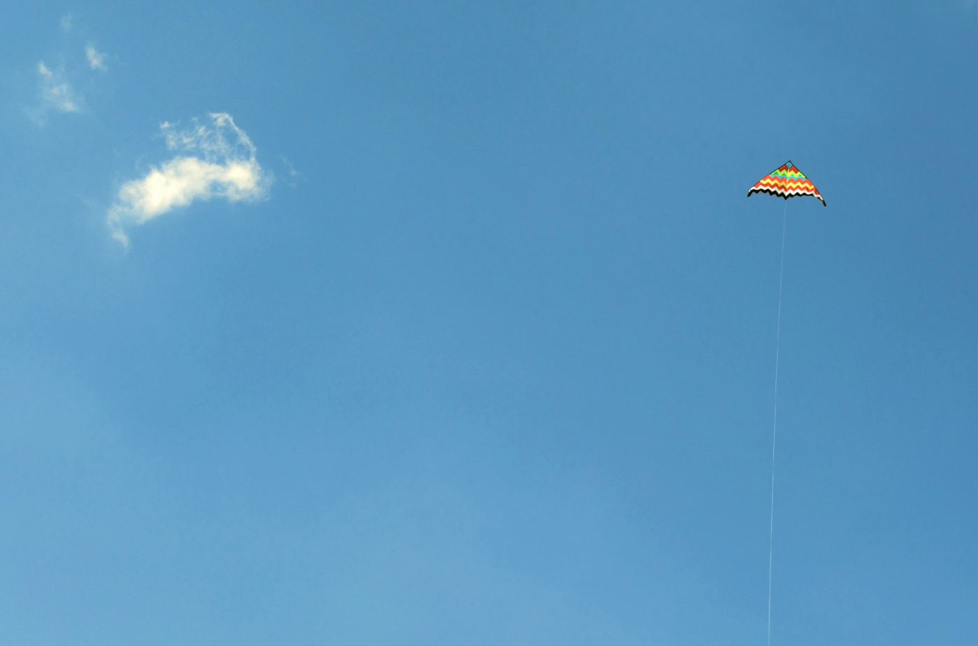 Blue sky, a small puffy cloud on the right, a colorful kite on a string on the left