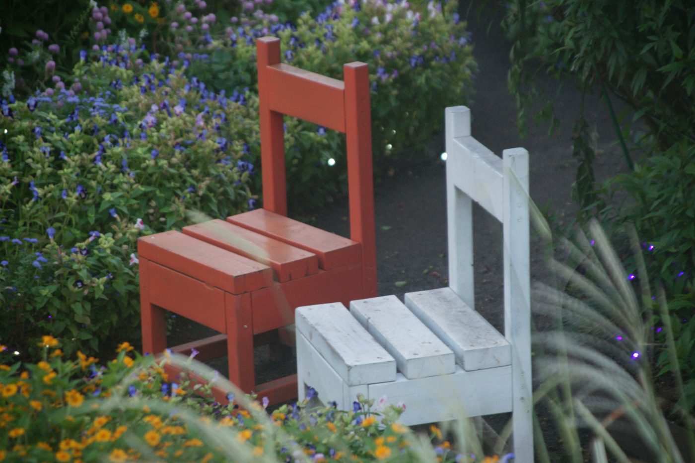 two simple wood chairs one white, one brown sitting empty in a garden
