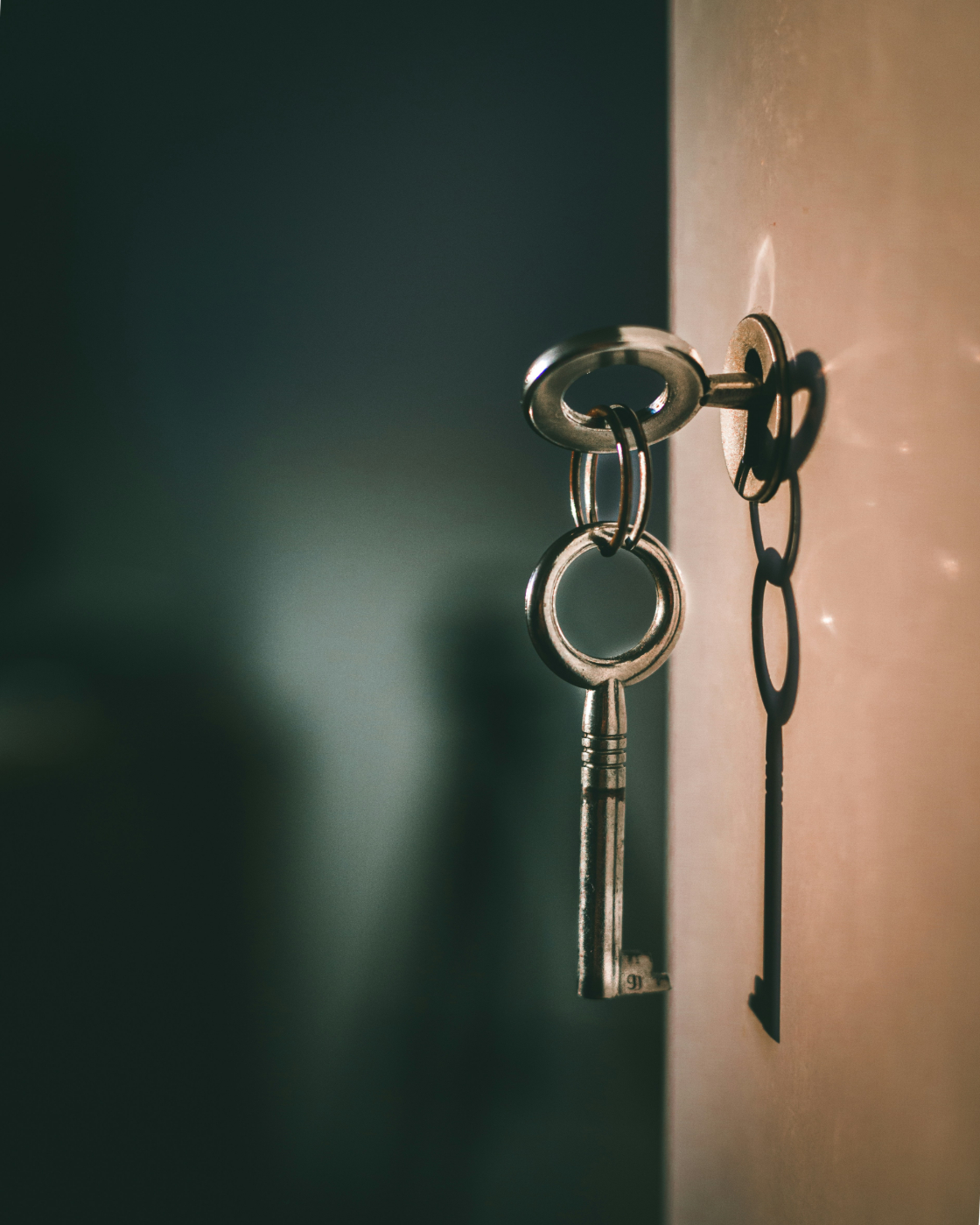 A skeleton key in a  lock with another dangling from it with the key's shadow on the wall