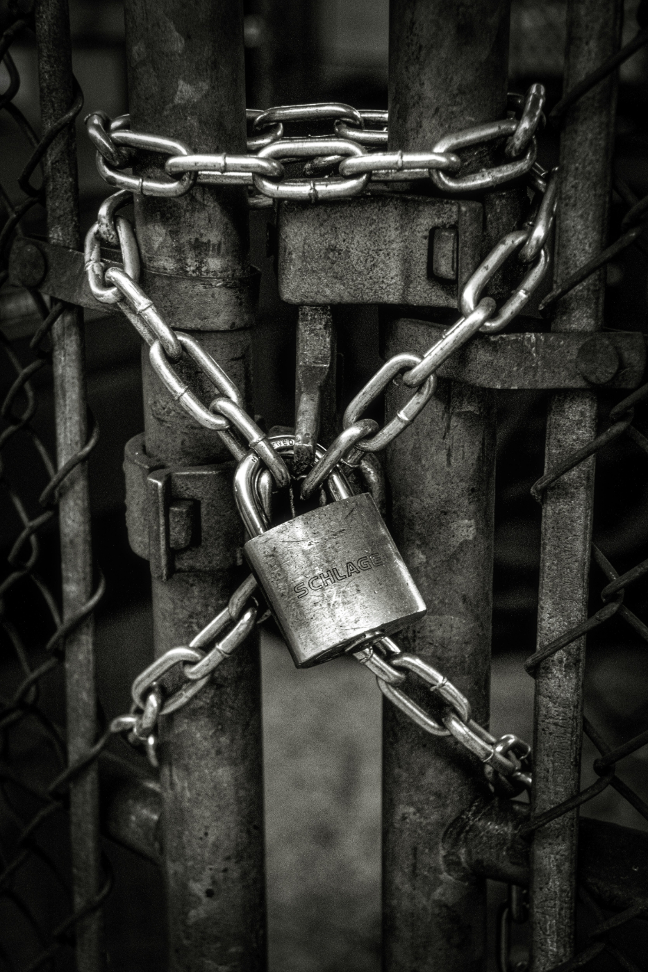 A gray scale image of a silver chain and a padlock securing a gate