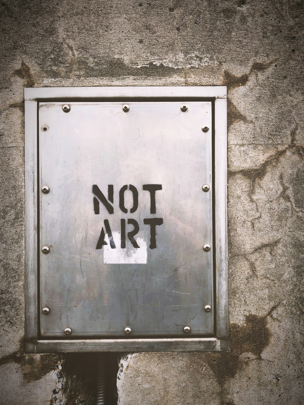 A steel panel in a stone wall with Not Art stenciled on it