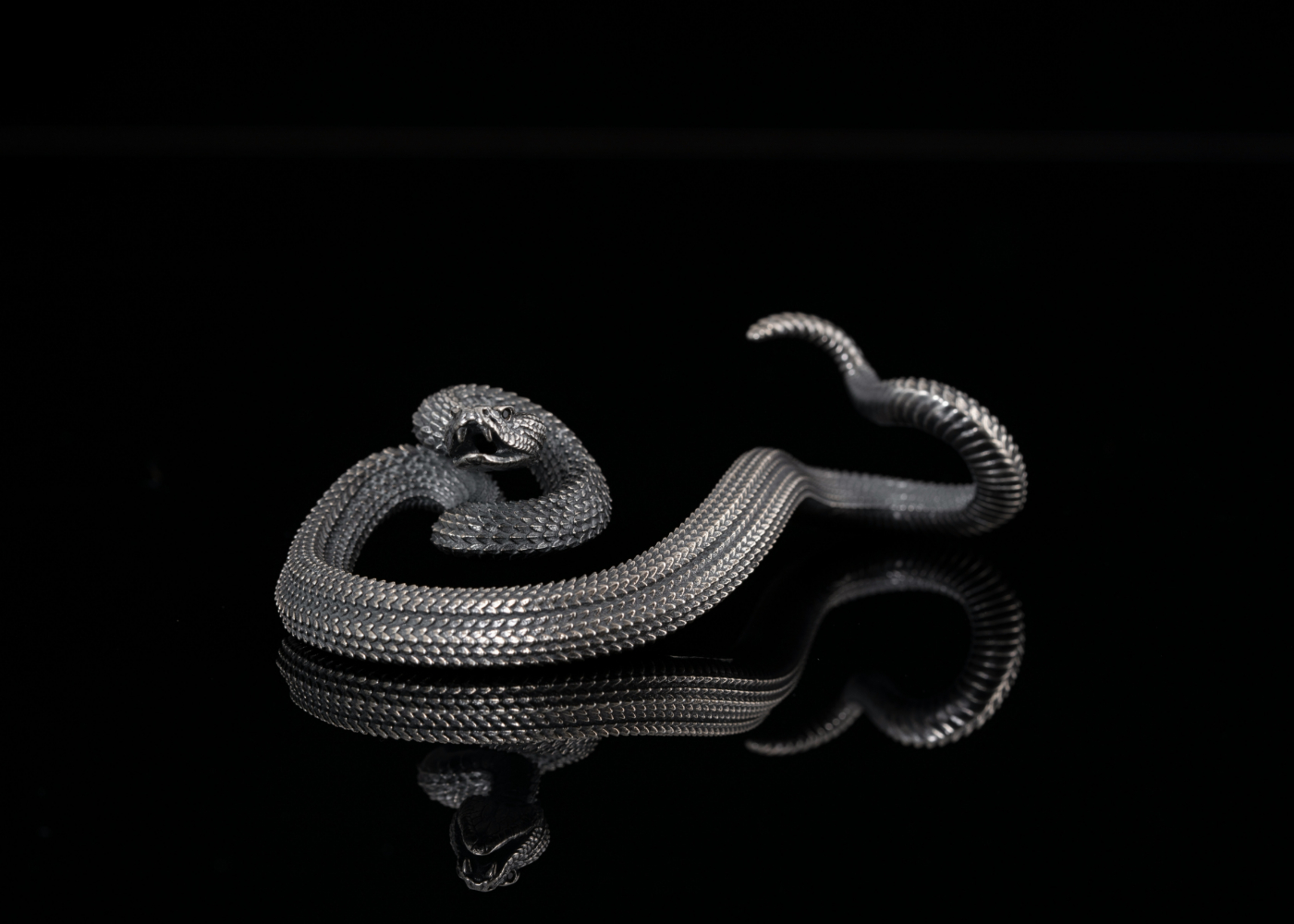 A silver statue of a rattle snake against a black background