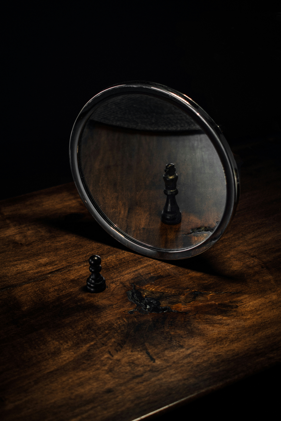 A chess pawn on a table in front of a mirror that is reflecting a king