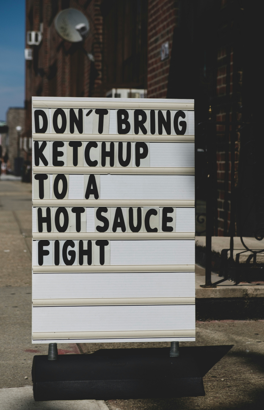 A street sign reading: Don't Bring Ketchup to a Hot Sauce Fight