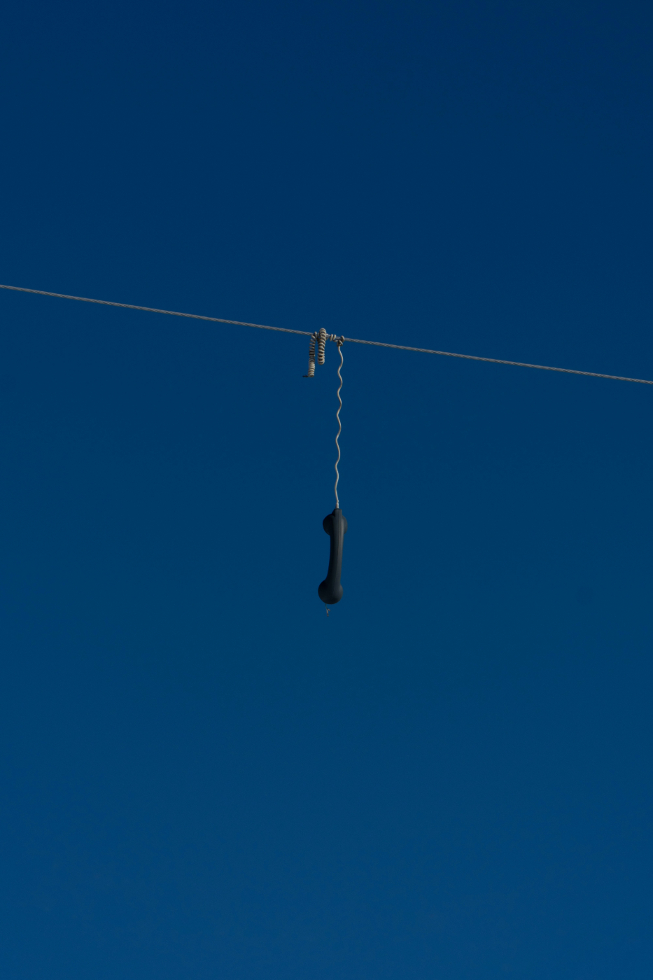 The handset of a phone with a cord hanging over a telephone wire