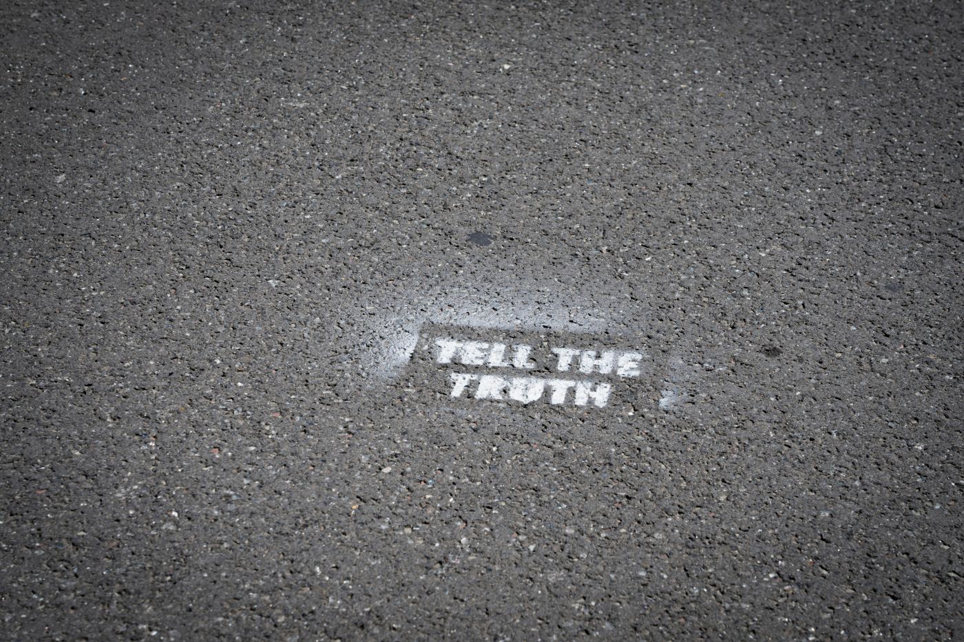 White paint stenciled on black asphalt reading Tell The Truth