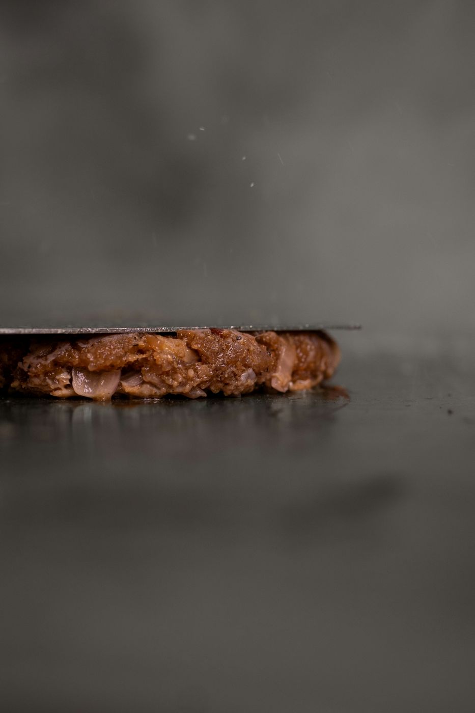 A bacon burger being flattened on a grill